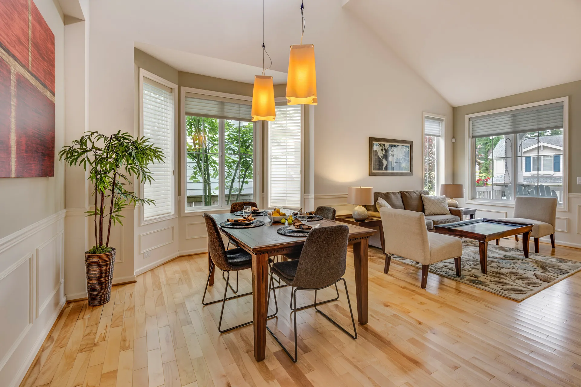 Dining area with wood table set for meal, hanging lights, chairs, plants, and big windows