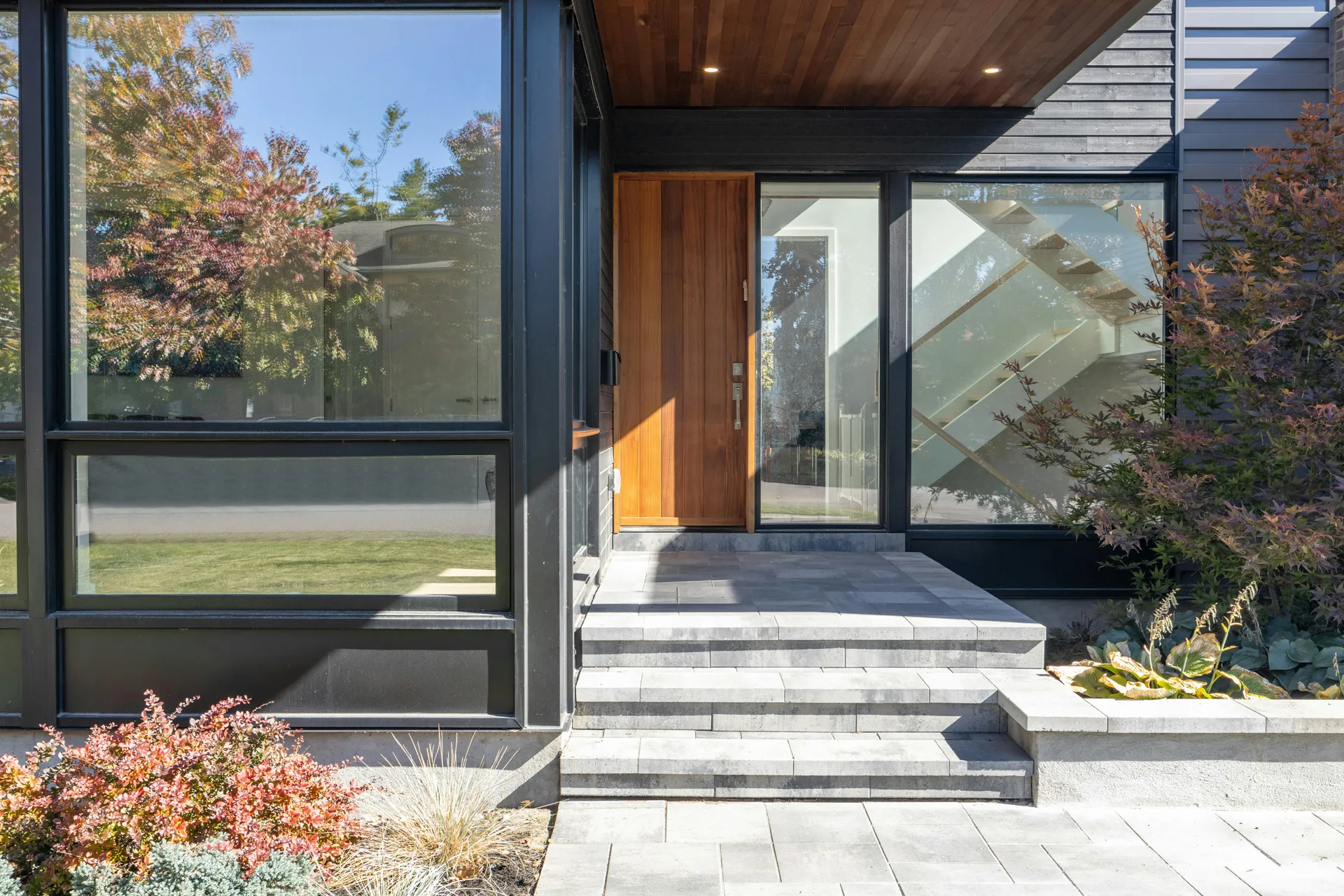 California real estate house entrance with wood door, big glass windows, green plants, and stone steps