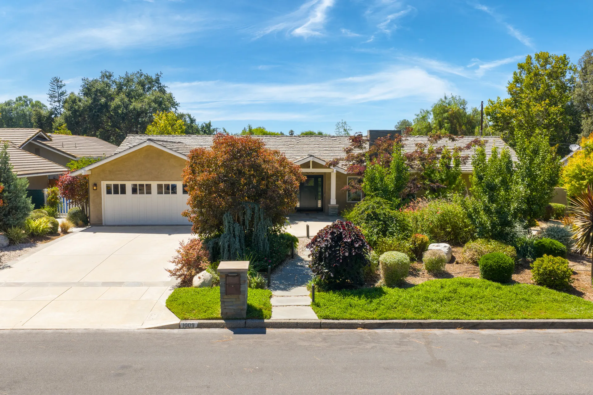 Real estate house aerial view with landscaped yard, plants, trees, driveway, and garage